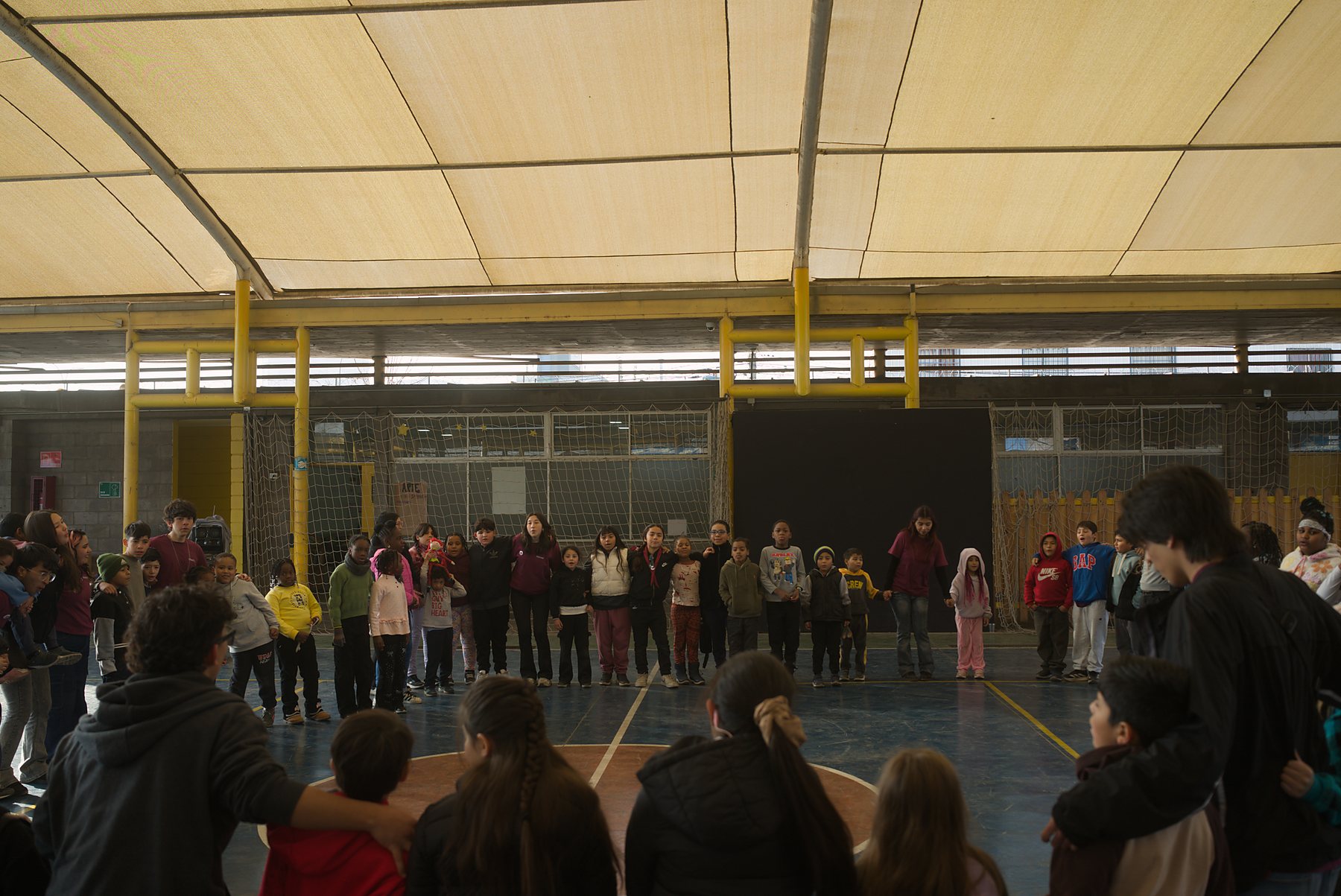 La ronda completa de niñas, niños y monitores en el patio techado, al comienzo de la jornada