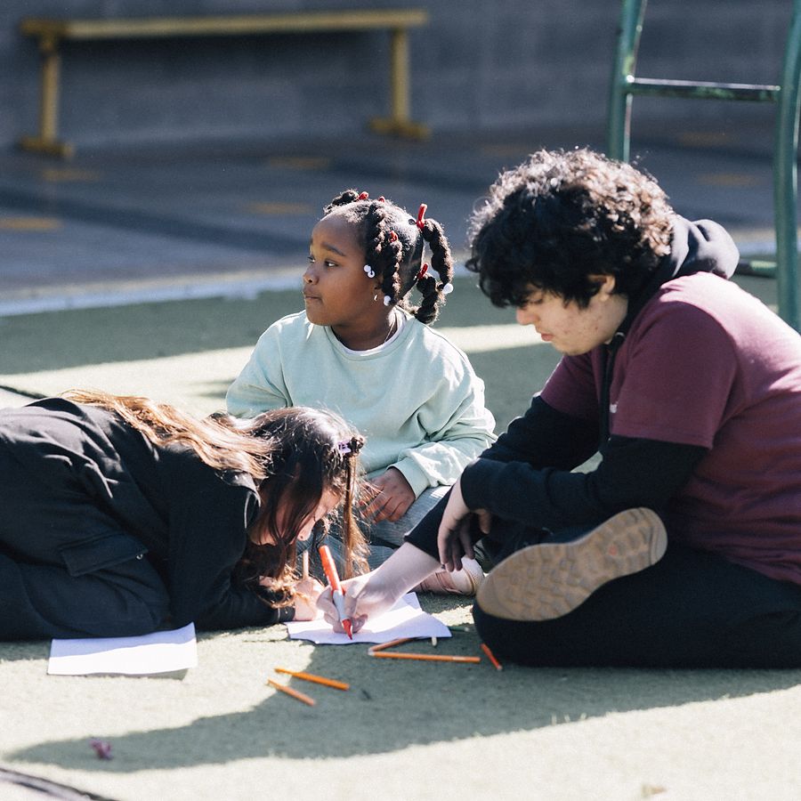 Niñas y niños dibujando sentados en el suelo del patio