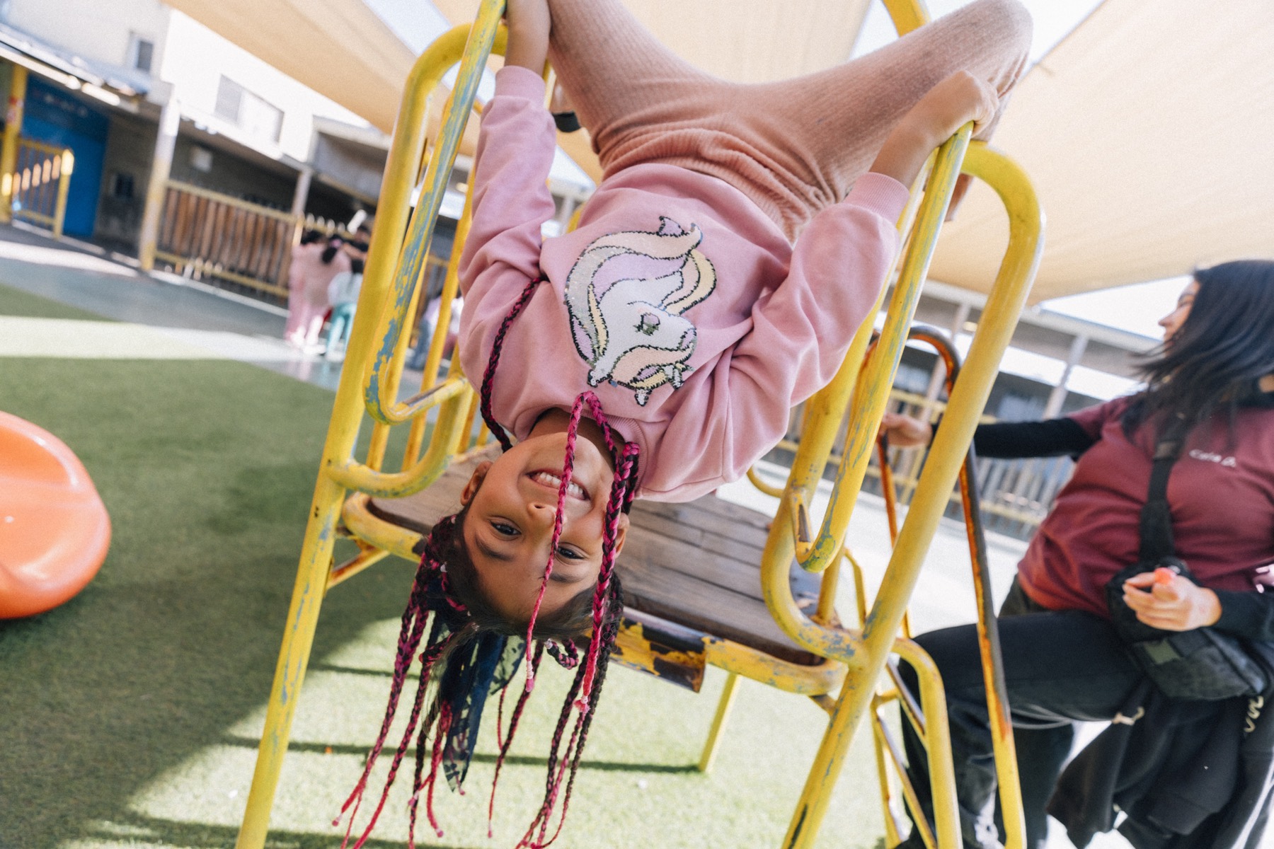 Niña colgando de cabeza de una estructura del patio
